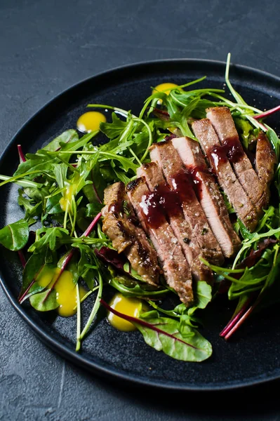 Salad with beef tenderloin, arugula and chard on a black plate. Side view, black background