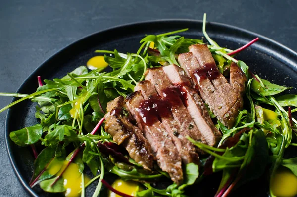 Salad with beef steak, arugula and chard on a black plate. Side view, black background, close up
