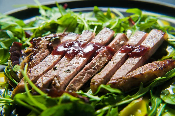 Salad with beef steak, arugula and chard on a black plate. Side view, black background, close up