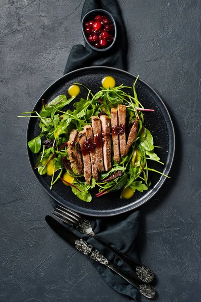 Sığır eti biftek, roka ve siyah bir tabak pazı salatası. Kızılcık sosu. Üstten Görünüm, siyah arka plan