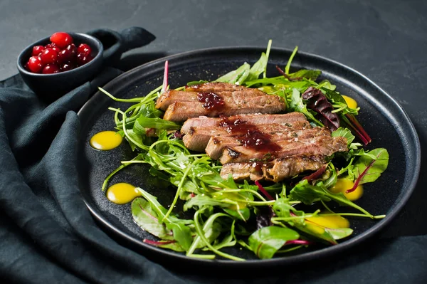 Salad with beef steak, arugula and chard on a black plate. Cranberry sauce. Top view, black background, close up