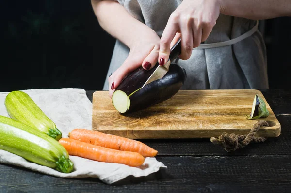 Elinde Şef ahşap kesme tahtası üzerinde patlıcan dilim. Yan görünüm, siyah arka plan, kapat