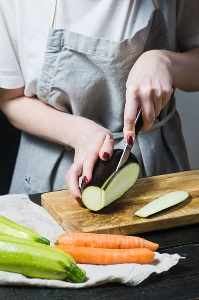Elinde Şef ahşap kesme tahtası üzerinde patlıcan dilim. Yan görünüm, siyah arka plan, kapat