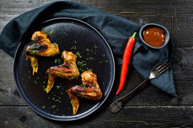 Tavuk kanadı üzerinde siyah bir tabak ızgara. Siyah ahşap arka plan, yan görünüm