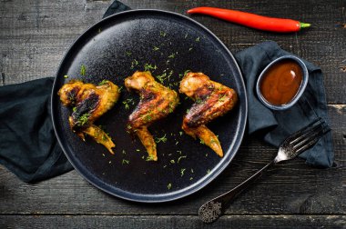 Tavuk kanadı Barbekü siyah plaka üzerinde. Siyah ahşap arka plan, yan görünüm
