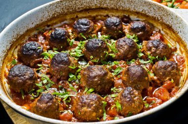 İsveç köftesi domates soslu bir pişirme çanağı içinde. Siyah arka plan, üstten görünüm, yakın çekim