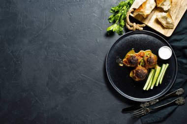 İsveç köftesi domates soslu bir siyah plaka, salatalık, tuz, ekmek. Siyah arka plan, üstten görünüm, metin için yer