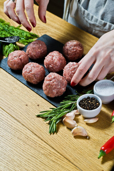 A female chef prepares Swedish meatballs from raw minced meat. Black background, top view, kitchen