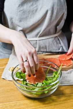 Kadın Şef salata roka yaprakları ile hazırlar. Siyah arka plan, yan görünüm, mutfak