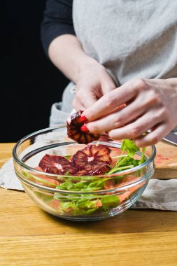 Şef koyar kırmızı portakal dilimlerini salata, bir kapta yemek. Siyah arka plan, yan görünüm, mutfak