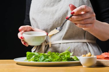 Şef roka yaprakları pişmiş bir plaka üzerinde ortaya konuyor. Siyah arka plan, yan görünüm, mutfak