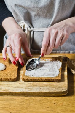 Şef, bir sandviç siyah ekmek hazırlar sos tost smear. Siyah arka plan, yan görünüm, mutfak