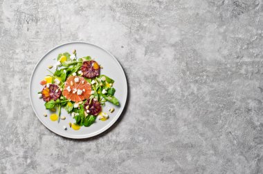 Roka, greyfurt, kırmızı portakal, fındık ve peynir salatası. Gri arka plan, üstten görünüm, metin için yer