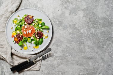 Roka, greyfurt, kırmızı portakal, fındık ve soya peyniri ile sağlıklı salata. Gri arka, yan görünüm