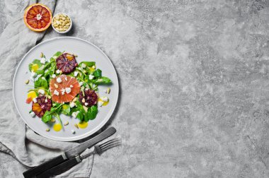 Roka, greyfurt, kırmızı portakal, fındık ve soya peyniri vejetaryen salatası. Gri arka plan, üstten görünüm, metin için yer