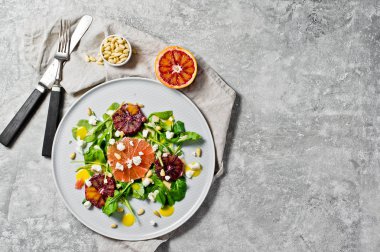 Roka, greyfurt, kırmızı portakal, fındık ve soya peyniri vejetaryen salatası. Gri arka plan, üstten görünüm, metin için yer