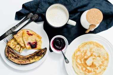 Kahvaltıda krep, böğürtlenli reçel, kızarmış muz ve kahve edilir. Beyaz arka plan, üstten görünüm, yakın çekim