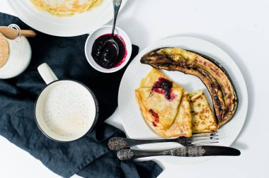 Kahvaltıda krep, böğürtlenli reçel, kızarmış muz ve kahve edilir. Beyaz arka plan, üstten görünüm, yakın çekim