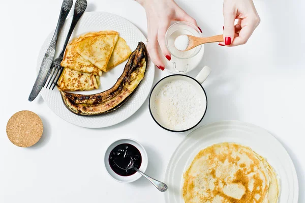 Kız bir fincan kahve, Kahvaltı krep ile bir kaşık dolusu şeker kamışı koyar. Beyaz arka plan, üstten görünüm, yakın çekim