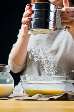 Şef glutensiz un bir kasenin içine sifts. Gluten free yemek ve laktoz ücretsiz pişirme kavramı. Malzemeler: Bıldırcın yumurta, şeker, glutensiz un, yulaf sütü. Siyah arka plan, yan görünüm, mutfak