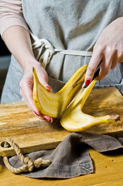 A chef cuts a banana into slices. Cooking baked bananas. Black background, side view, kitchen
