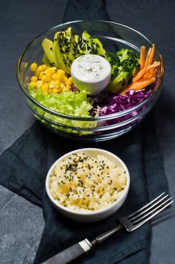 Vejetaryen yemek, salata kasesi. Malzemeler brokoli, Mısır, havuç, kuskus, marul, lahana, sos. Siyah arka plan, yan görünüm