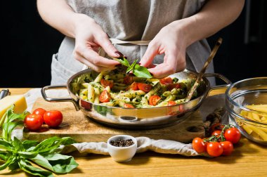 Şef fesleğen yaprakları üzerinde makarna Penne sprinkles. Siyah arka plan, yan bakış, metin için yer mutfak