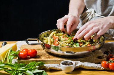 Şef fesleğen yaprakları üzerinde makarna Penne sprinkles. Siyah arka plan, yan bakış, metin için yer mutfak