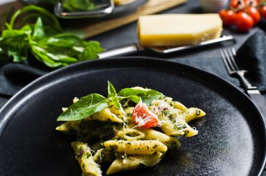 Ispanak, domates ve fesleğen ile İtalyan makarna Penne. Siyah arka plan, yan görünüm