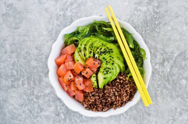 Poke kase. Malzemeler: somon, avokado, kahverengi pirinç, yosun. Gri arka plan, üstten görünüm, metin için yer