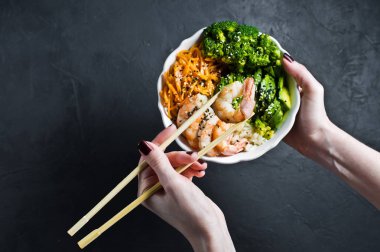 Buda kase tutan kız. Malzemeler: karides, avakado, havuç, brokoli ve pirinç. Siyah arka plan, üstten görünüm