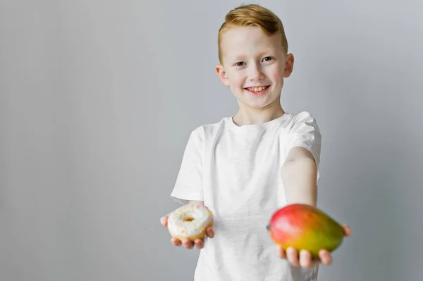Making a choice between healthy and unhealthy food. The child is holding a donut and mango