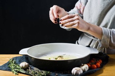 Şef pişirme çanağı biberiye ekler. Fırında patates pişirme kavramı. Siyah arka plan, yan bakış, metin için yer mutfak