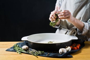 Şef pişirme çanağı biberiye ekler. Fırında patates pişirme kavramı. Siyah arka plan, yan bakış, metin için yer mutfak