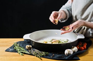 Şef pişirme çanağı sarımsak ekler. Fırında patates pişirme kavramı. Siyah arka plan, yan bakış, metin için yer mutfak