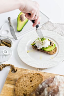 Şef haşlanmış yumurta sandviç avokado ve hamsi keser. Beyaz arka plan, üstten görünüm.