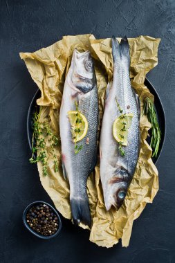 Biberiye, kekik ve limon ile Kraft kağıt üzerinde çiğ levrek. Siyah arka plan, üstten görünüm.