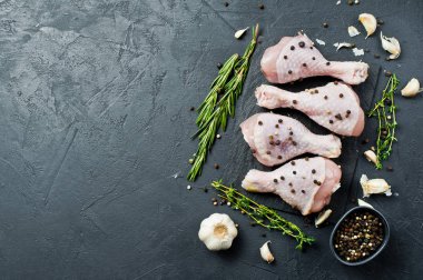 Çiğ tavuk budu. Yemek pişirmek için malzemeler: biberiye, kekik, sarımsak, biber. Siyah arka plan, üstten görünüm, metin için yer.