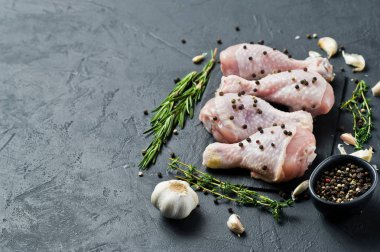 Çiğ tavuk budu. Yemek pişirmek için malzemeler: biberiye, kekik, sarımsak, biber. Siyah arka plan, üstten görünüm, metin için yer.