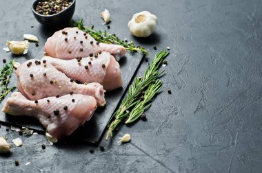 Tavuk bacağı çeyrek. Yemek pişirmek için malzemeler: biberiye, kekik, sarımsak, biber. Siyah arka plan, üstten görünüm, metin için yer.