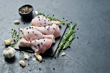 Tavuk bacağı çeyrek. Yemek pişirmek için malzemeler: biberiye, kekik, sarımsak, biber. Siyah arka plan, üstten görünüm, metin için yer.