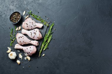 Tavuk bacağı çeyrek. Yemek pişirmek için malzemeler: biberiye, kekik, sarımsak, biber. Siyah arka plan, üstten görünüm, metin için yer.