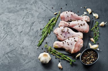 Tavuk bacağı çeyrek. Yemek pişirmek için malzemeler: biberiye, kekik, sarımsak, biber. Siyah arka plan, üstten görünüm, metin için yer.