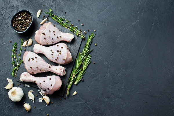 Çiğ tavuk budu. Yemek pişirmek için malzemeler: biberiye, kekik, sarımsak, biber. Siyah arka plan, üstten görünüm, metin için yer.
