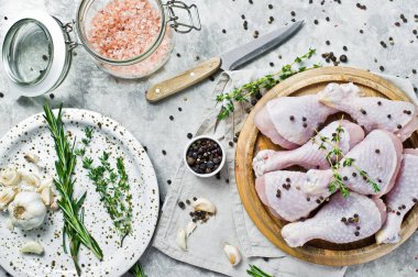 Çiğ tavuk budu. Yemek pişirmek için malzemeler: biberiye, kekik, sarımsak, biber. Gri arka plan, üstten görünüm.