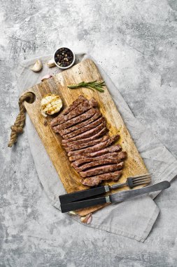 Ahşap doğrama tahtası üzerinde Barbekü biftek dilimlenmiş. Gri arka plan, üst 