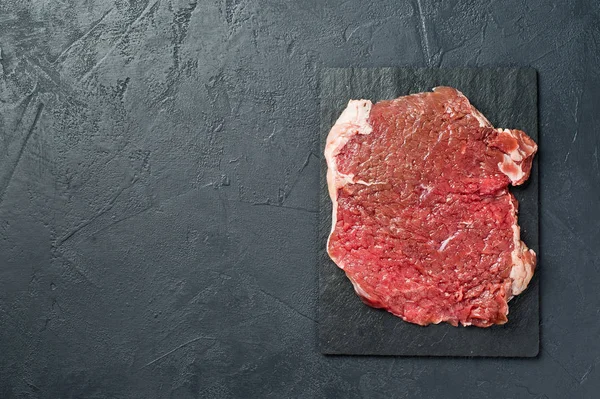 Beef flank steak on a stone Board. Black background, top view, s