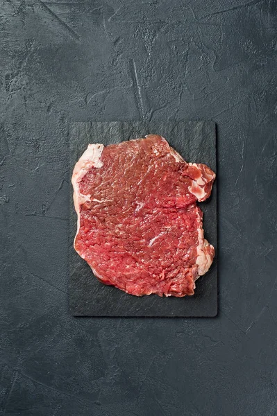 Beef flank steak on a stone Board. Black background, top view, s