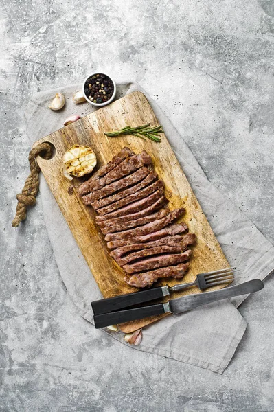 Ahşap doğrama tahtası üzerinde Barbekü biftek dilimlenmiş. Gri arka plan, üst 