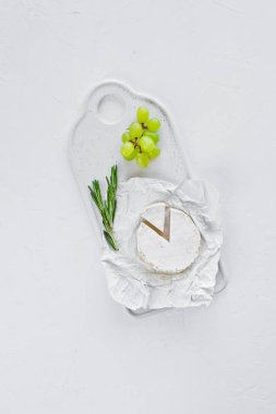 Beyaz bir kesme tahtasında camembert peyniri, üzüm, biberiye. Wh